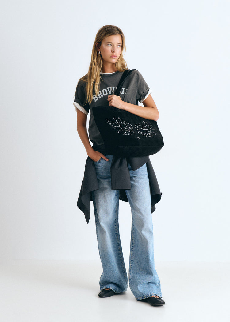 Bolso shopper negro con diseño de alas decoradas con tachas lucido sobre el hombro