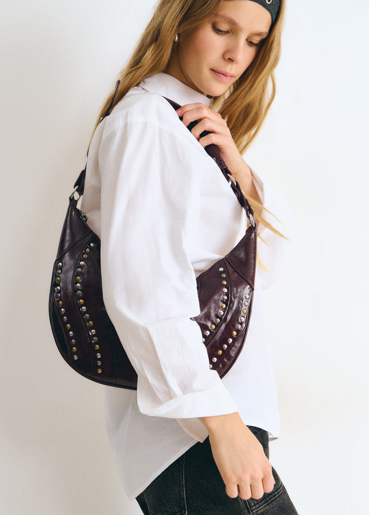 Bolso de hombro en tono granate con remates de tachas metálicas visto de perfil