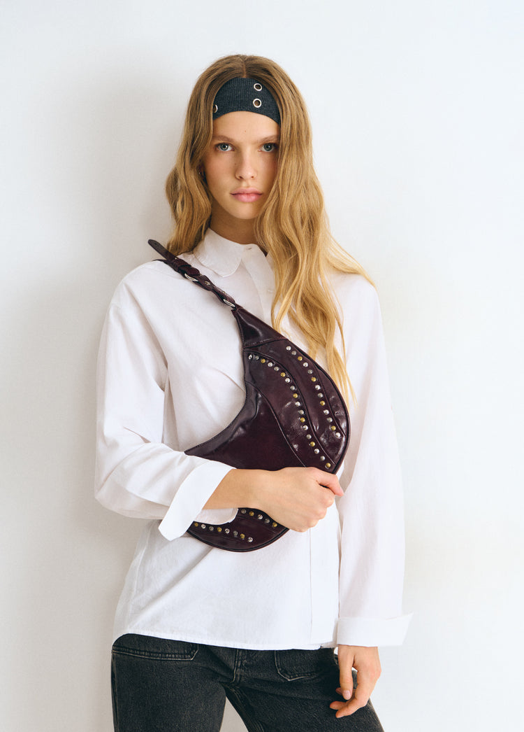 Bolso de hombro en tono granate con remates de tachas doradas luciendo su perfil curvo