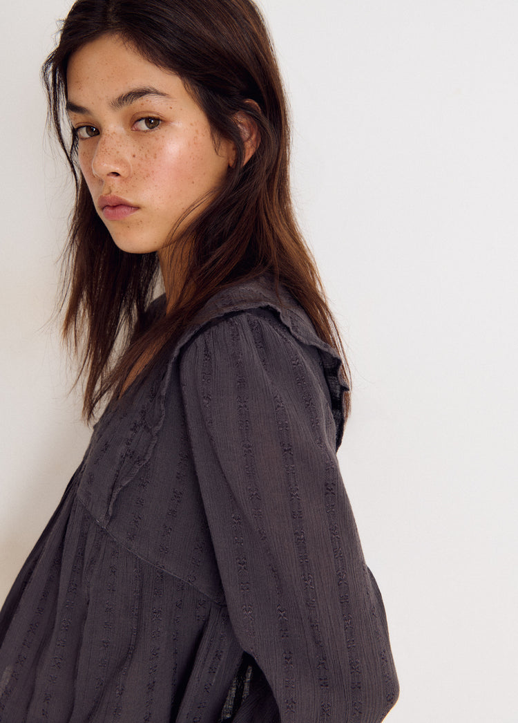 Blusa de manga larga en gris con textura de picot y cuello con volantes vistos desde el lateral