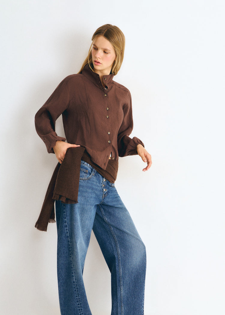 Blusa marrón de cuello alto y manga larga lucida con un nudo lateral sobre vaqueros