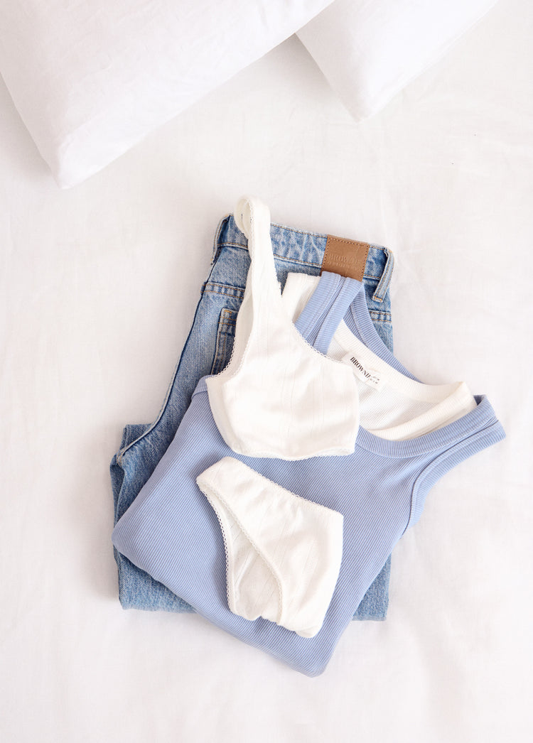 Pack íntimo de dos braguitas y top en color crudo sobre vaqueros y camiseta azul