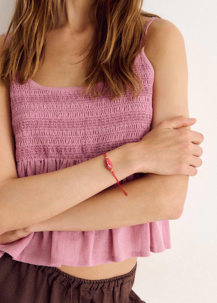 Pulsera roja de pez decorativo lucida en la muñeca con los brazos cruzados