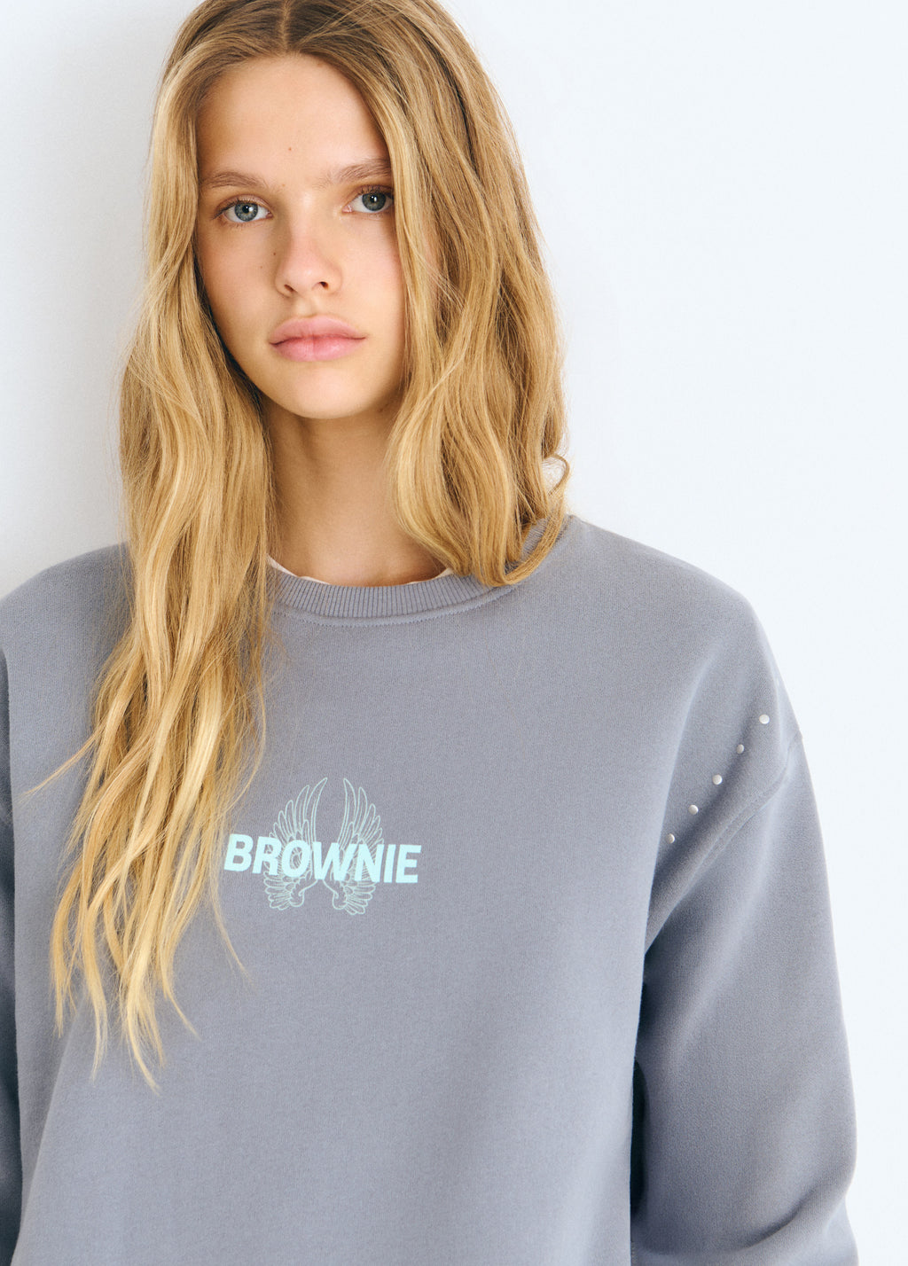 Sudadera gris con estampado de alas glitter y detalles de perforaciones en la manga