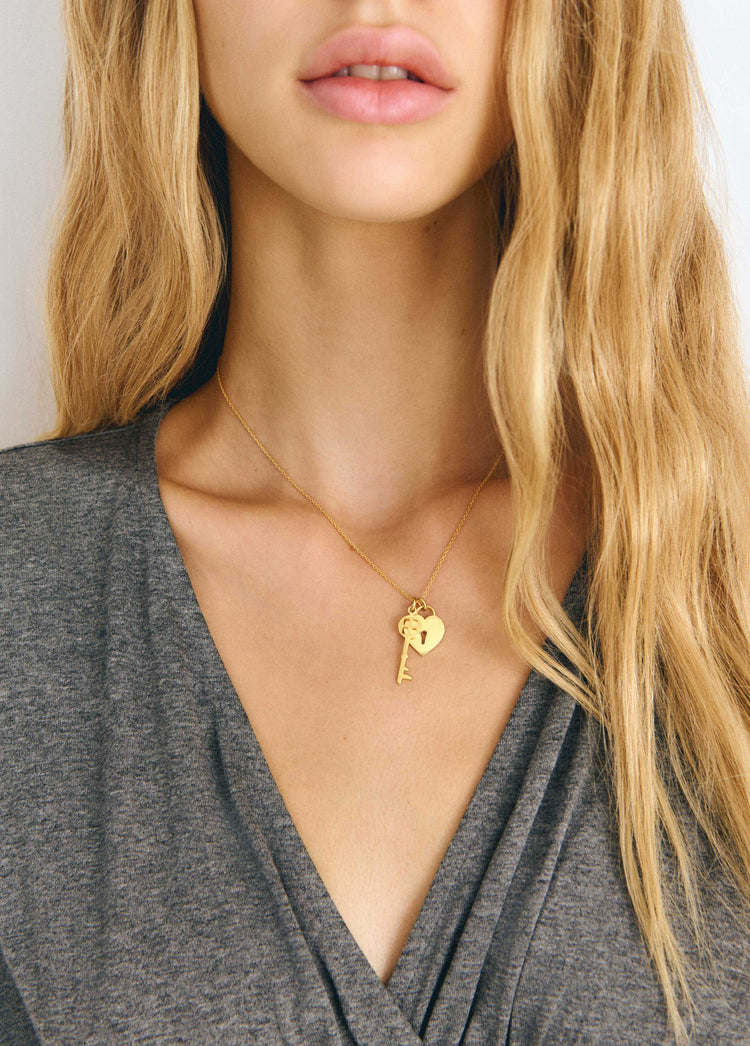 Collar de cadena fina dorada con colgantes de llave y corazón sobre el pecho