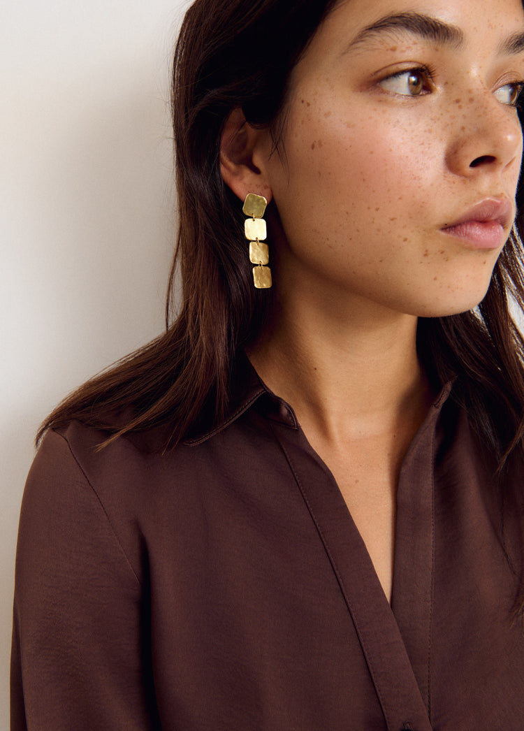 Pendientes cuadrados colgantes de color dorado vistos en perfil sobre la oreja