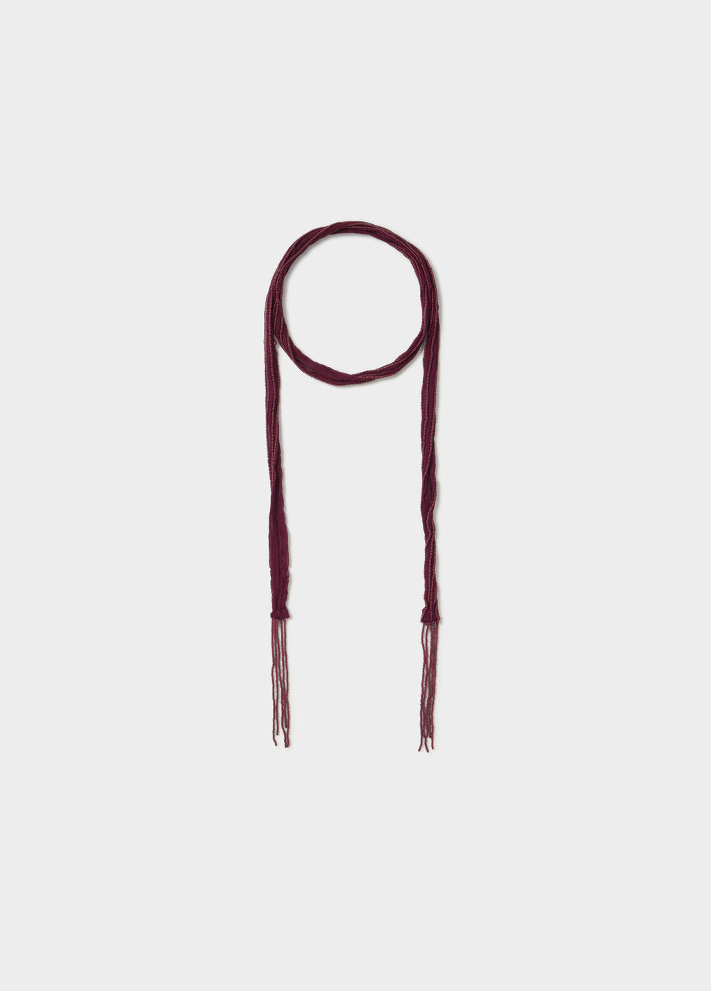 Collar bordado de color granate con extremos trenzados y flecos colgando sobre fondo liso