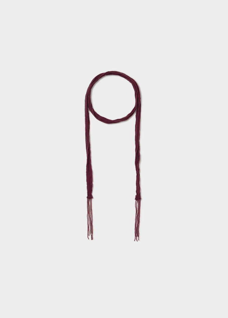 Collar bordado de color granate con extremos trenzados y flecos colgando sobre fondo liso