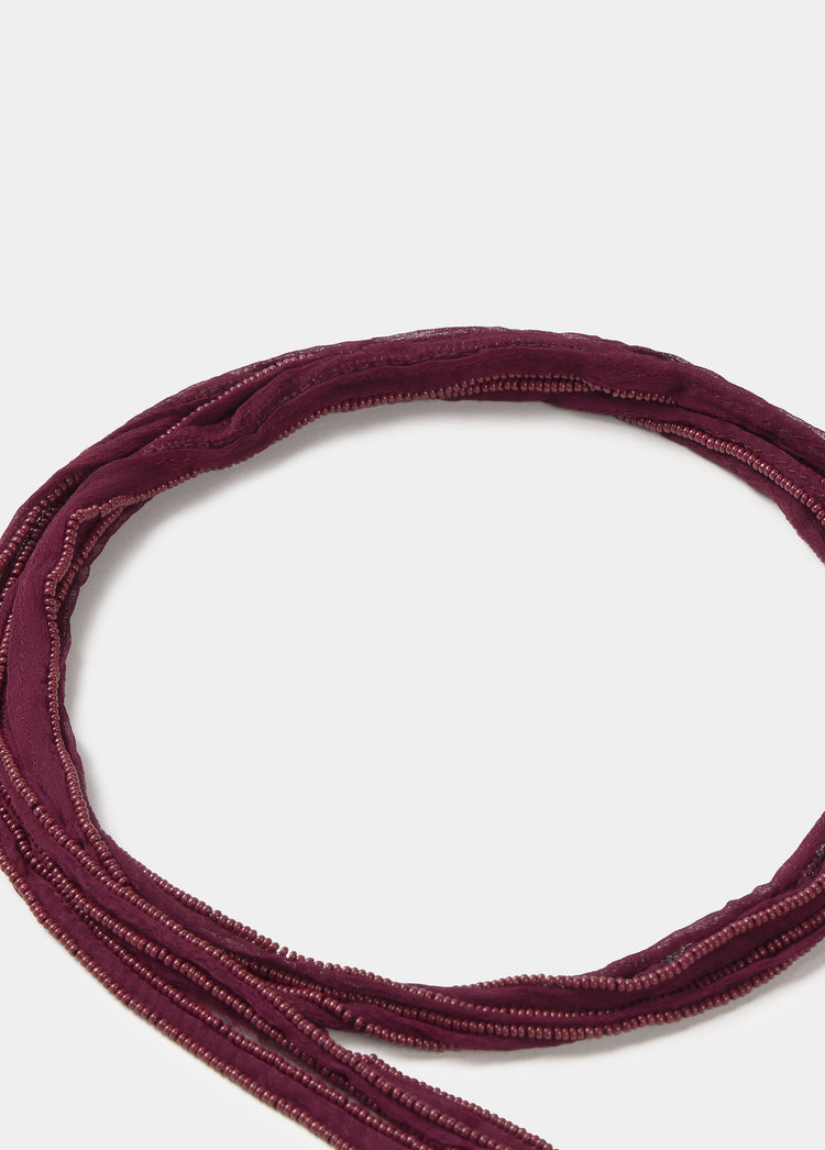 Collar de hilo bordado en tono granate fotografiado en plano cenital sobre fondo liso