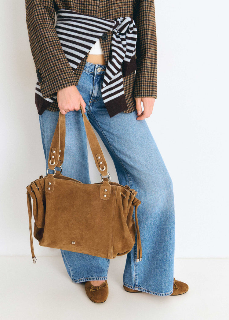 Bolso shopper de ante fruncido en color camel colgado de la mano sobre modelo