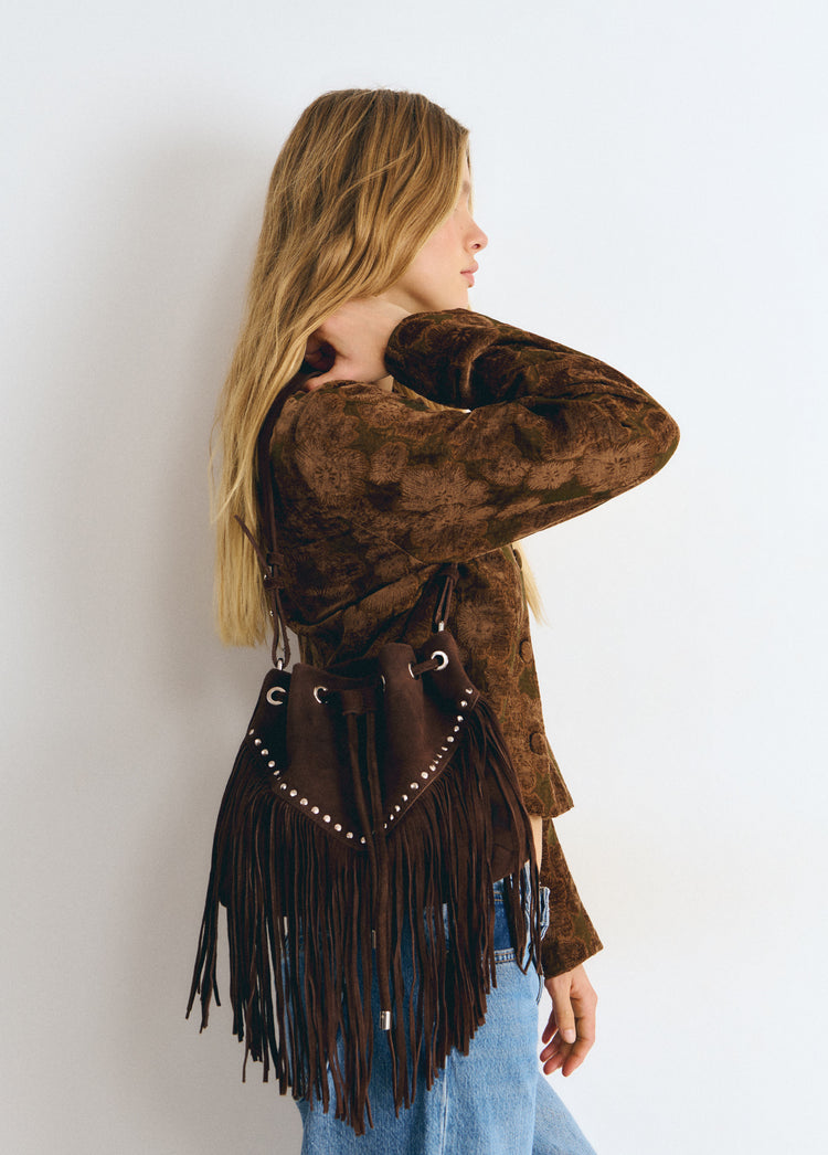 Bolso saco de color marrón con flecos y remaches, visto de perfil sobre el hombro