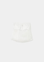 Top bandeau blanco de tirante fino con botones frontales y costuras verticales, lucido sobre fondo de rocas marinas