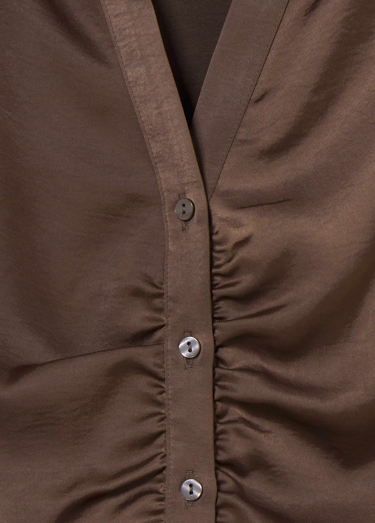 Blusa satinada de color marrón con detalle de frunce y botones metálicos en el cierre frontal