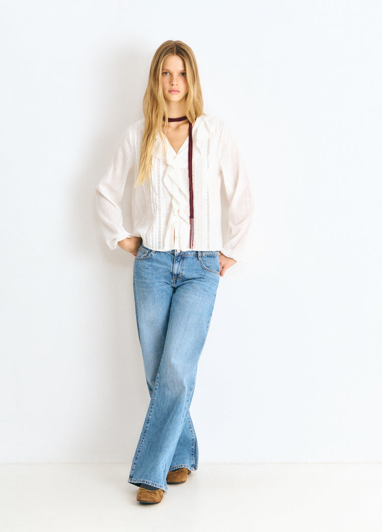 Blusa blanca de manga ancha y volante central lucida en vista frontal completa