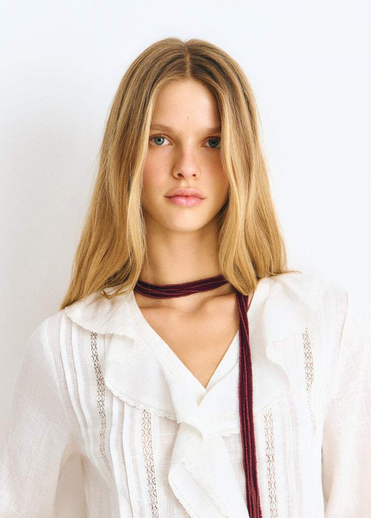 Blusa blanca de cuello abierto con volantes y bordado central luciendo su caída frontal