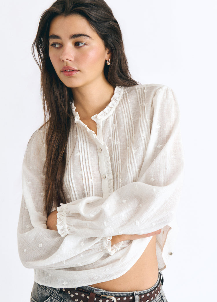 Blusa blanca de manga larga con jaretas y detalles lurex luciendo el dobladillo despegado