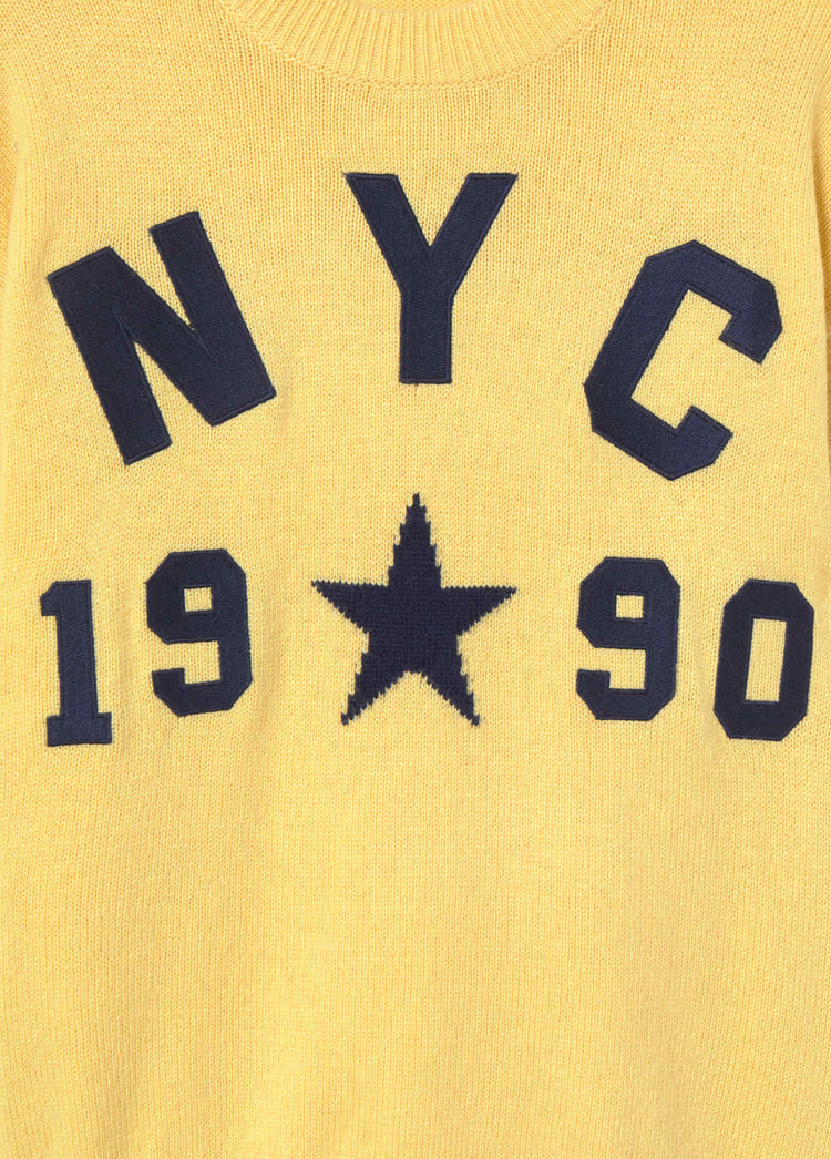 Primer plano del jersey de punto en mostaza mostrando el detalle del diseño de letras y estrella