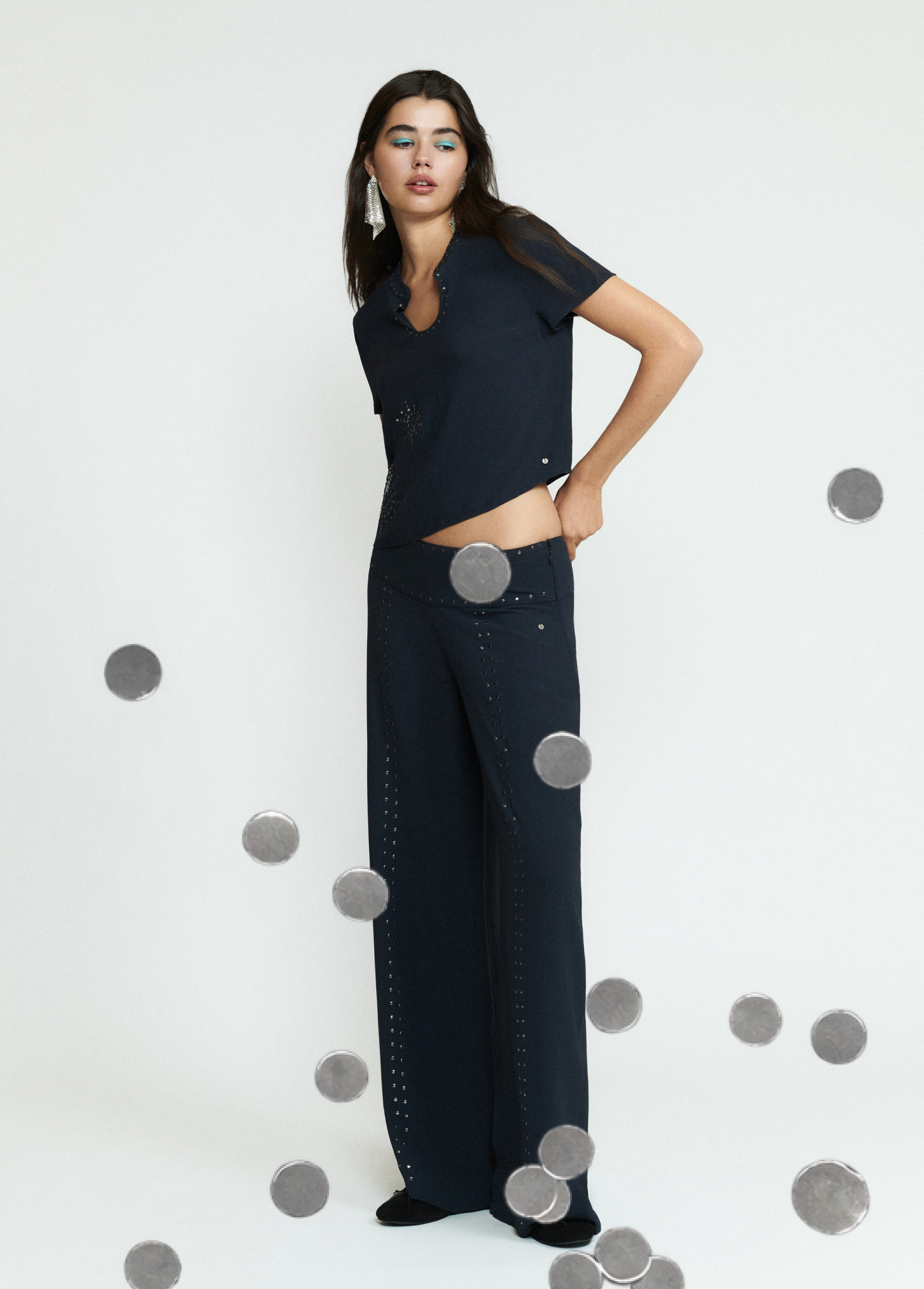 Pantalón largo negro de corte amplio con detalles de tachas sobre modelo
